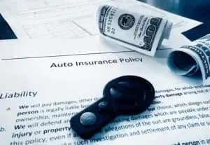 A car key, rolled-up cash, and paperwork labeled “Auto Insurance Policy” are shown on a table, symbolizing car insurance and financial planning.