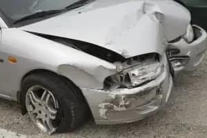 A silver car with significant damage to its front bumper and hood, indicating a recent collision. The front right headlight is broken, and another vehicle is visible next to it.