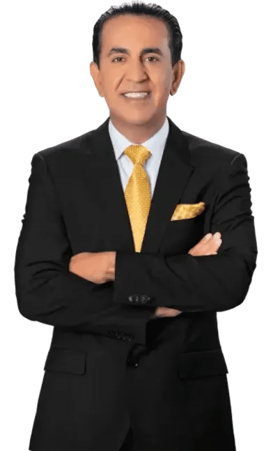 A man in a black suit with a white shirt and yellow tie stands with arms crossed, smiling at the camera. He also has a yellow pocket square.
