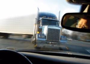 View from inside a car as a large semi-truck approaches head-on at high speed, evoking the danger of car accidents. A person’s reflection is visible in the rearview mirror, highlighting moments that may require a personal injury attorney.